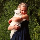 Blonde Woman Embracing White Dog in Green Setting