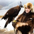 Mongolian Eagle Hunter in Traditional Attire with Bird and Mountains