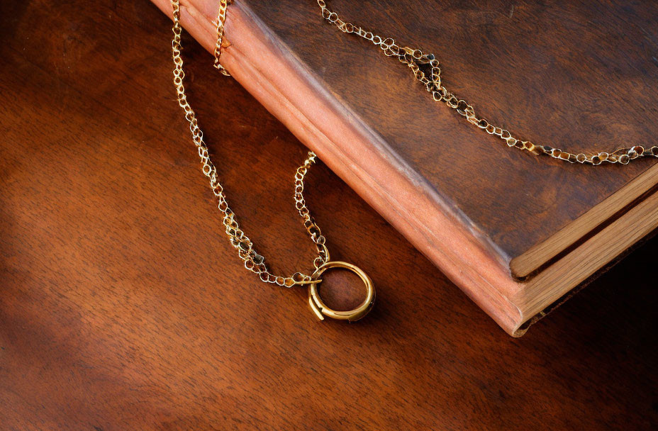Gold Necklace with Ring Pendant on Wooden Surface Next to Closed Book