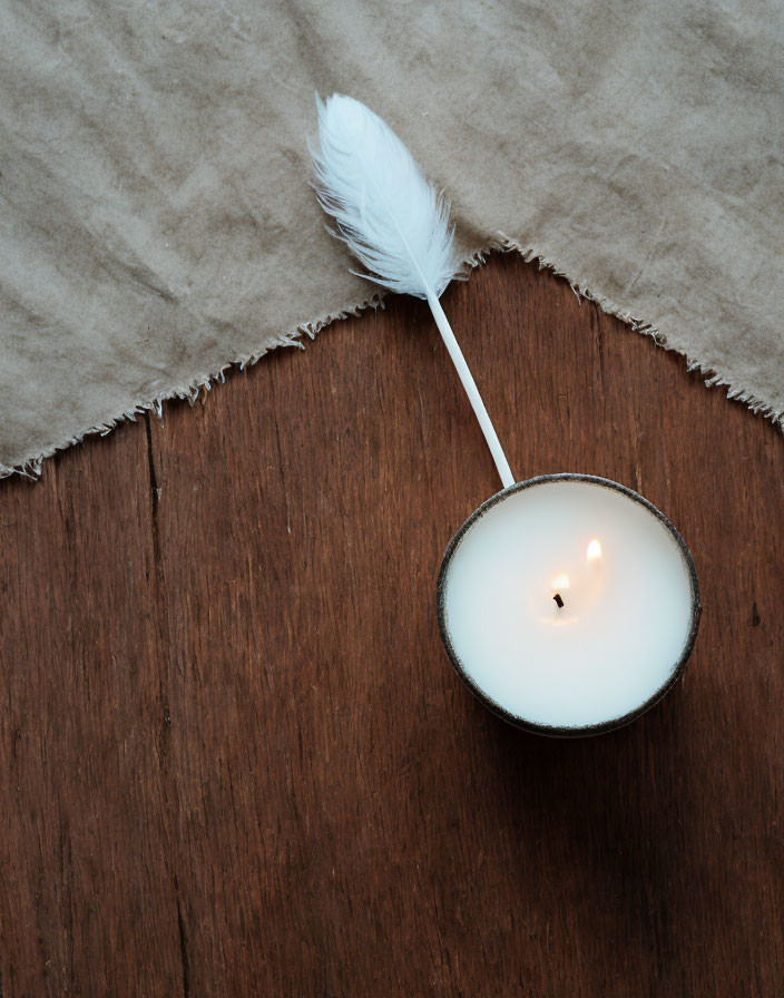 Candle in Holder with Feather on Wooden Surface