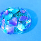 Transparent Bowl with Submerged Flowers Reflecting Colorful Light on Blue Surface