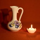White porcelain pitcher with floral designs on orange fabric next to tealight candle