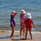 Three girls in colorful swimsuits and sunhats by the shore.