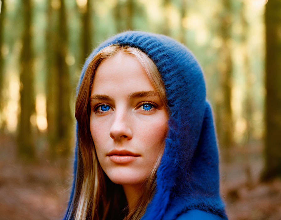 Blue-eyed woman in blue hood gazes at camera in forest setting