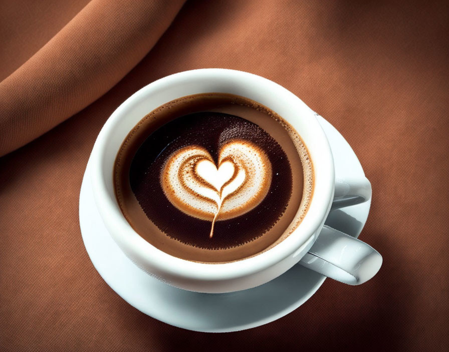 Heart-shaped latte art on cup of coffee on saucer with brown cloth background
