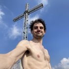 Muscular male figure holding metallic cross under blue sky