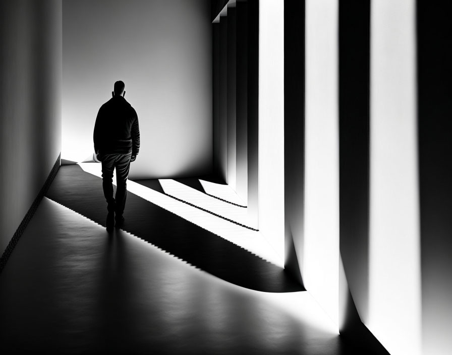 Solitary figure in corridor with geometric light and shadow patterns