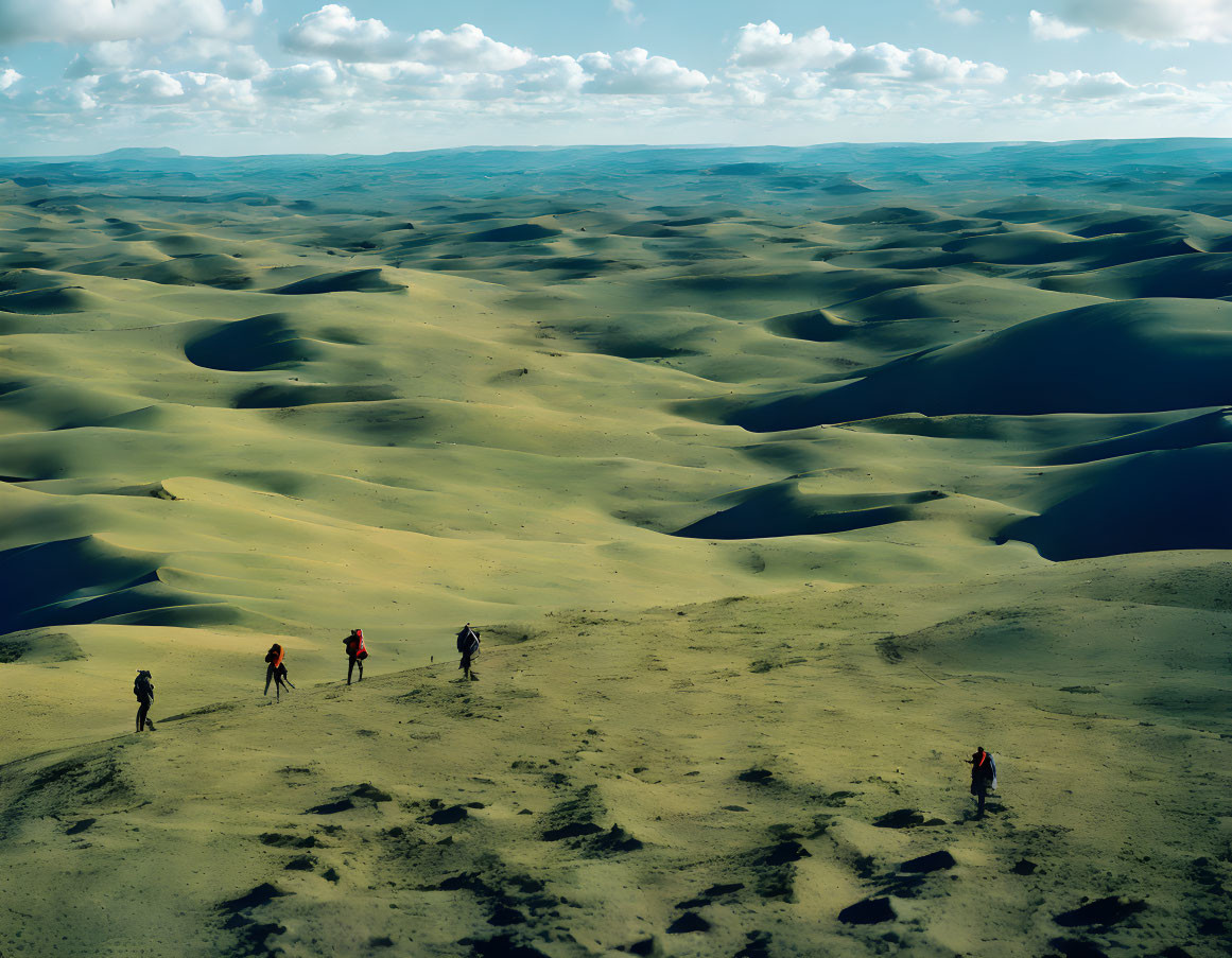 Hikers exploring vast sand dunes under cloudy sky
