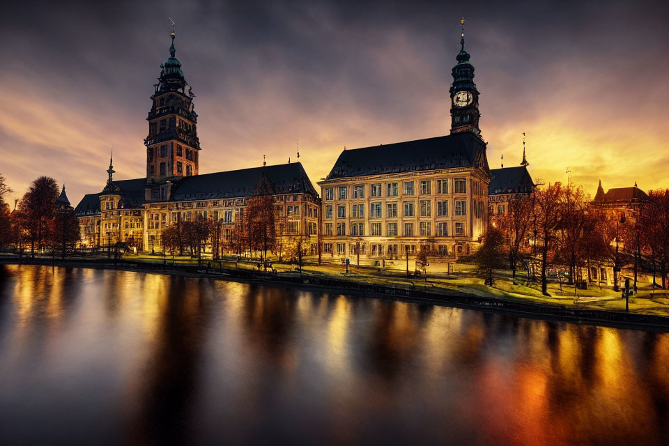 Historic building with tall spires by calm river at golden sunset