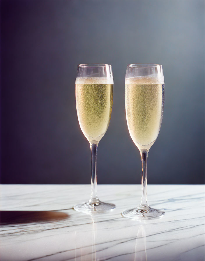 Sparkling champagne flutes on marble surface with dark background.