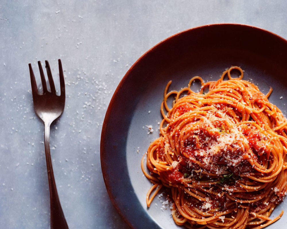 Plate of spaghetti with tomato sauce and parmesan cheese on dark background