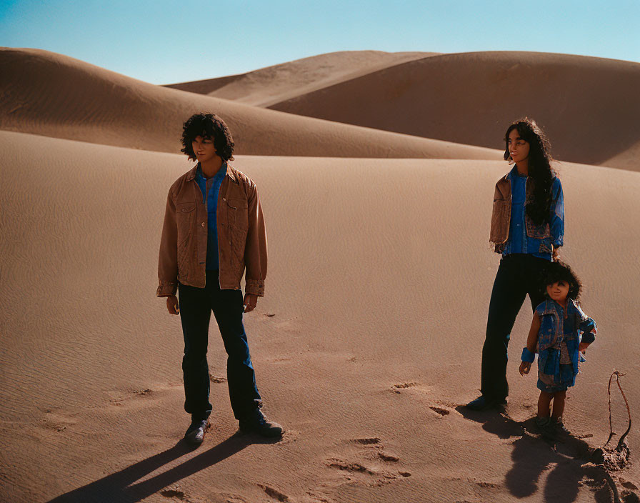 Three people in desert with sand dunes, wearing casual attire