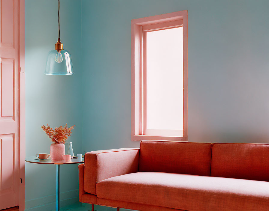 Pink sofa, green side table, plant, lamp, and window in a room with soft blue walls