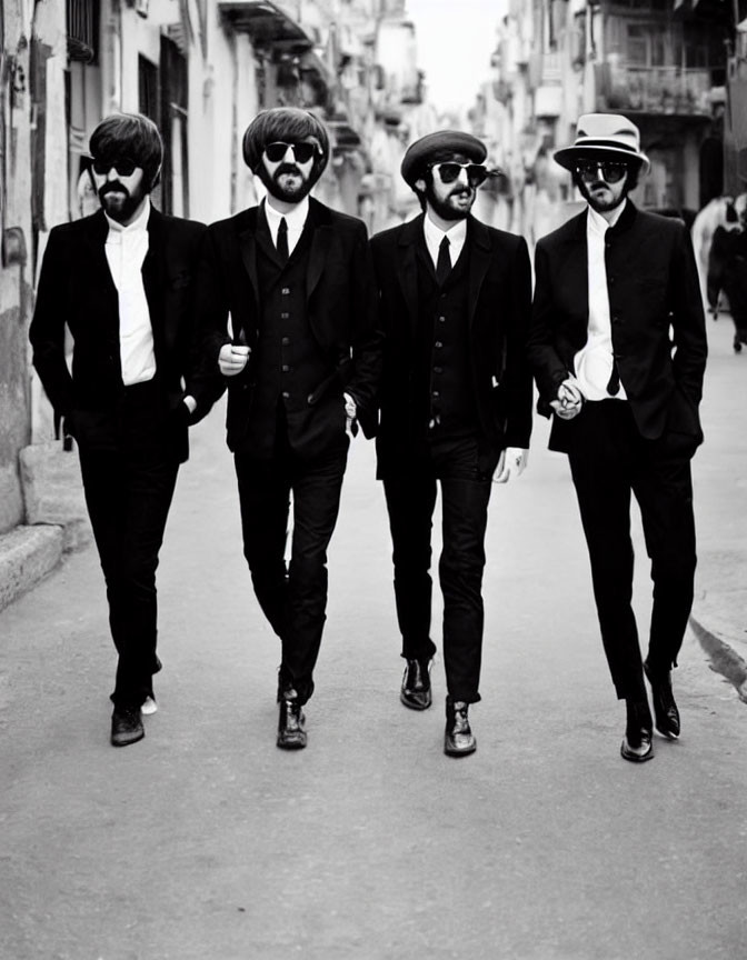 Four men in black suits with sunglasses and unique hats walking in urban setting