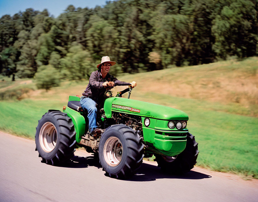 Cowboy hat man rides vintage green John Deere tractor on country road.