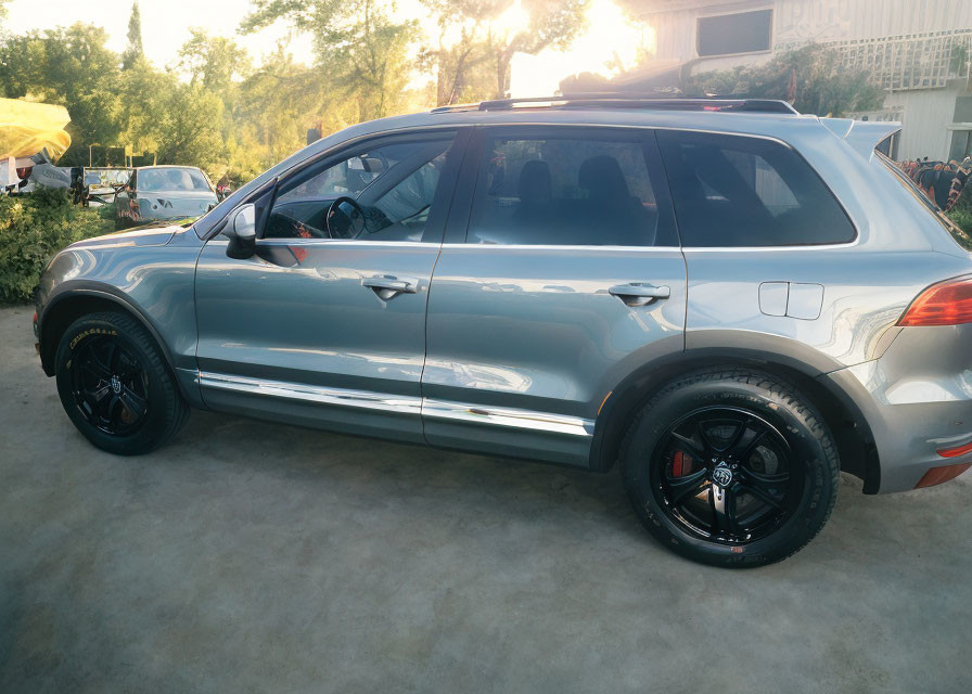 Silver SUV with Black Rims and Open Door, Outdoor Setting with Trees and Building