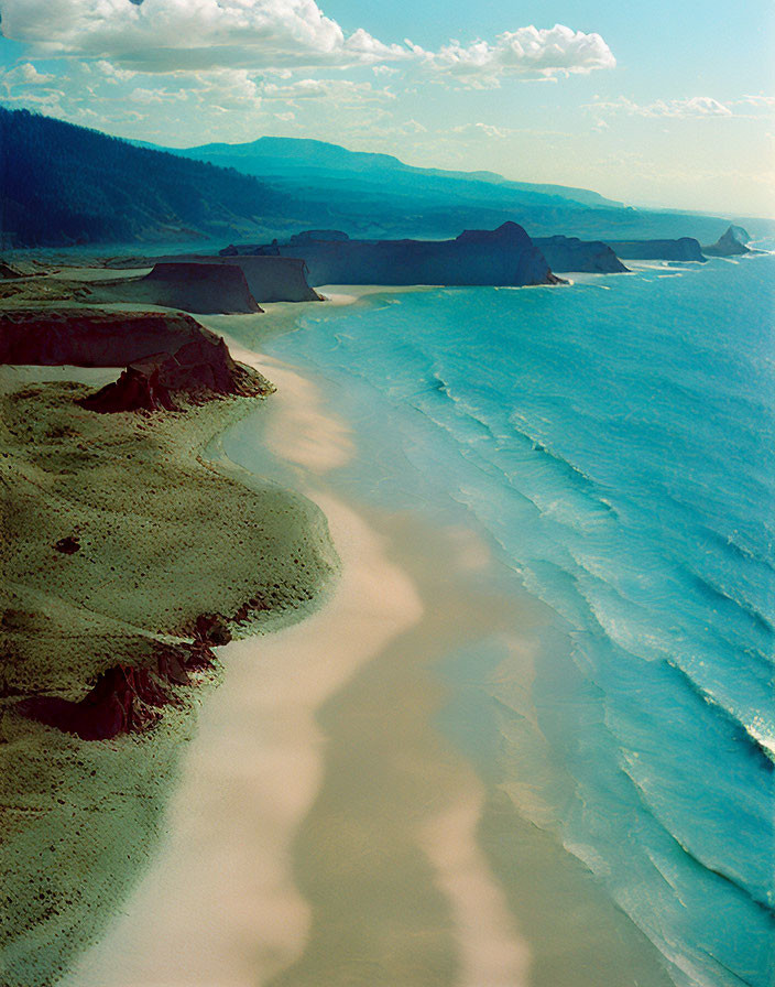 Scenic aerial view of sandy beach, blue ocean, and rocky headlands