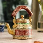 Colorful ornate kettle with gold accents, oranges, and flowers on wooden table