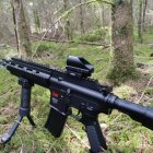 Black Assault Rifle with Scope, Extended Magazine, and Foregrip in Forest Setting