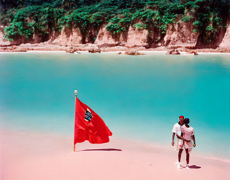 Red Flag with Crest on Sandy Beach with Two People by Turquoise Waters
