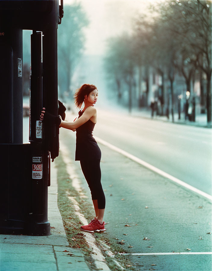 Athletic woman leaning on telephone booth in misty street.