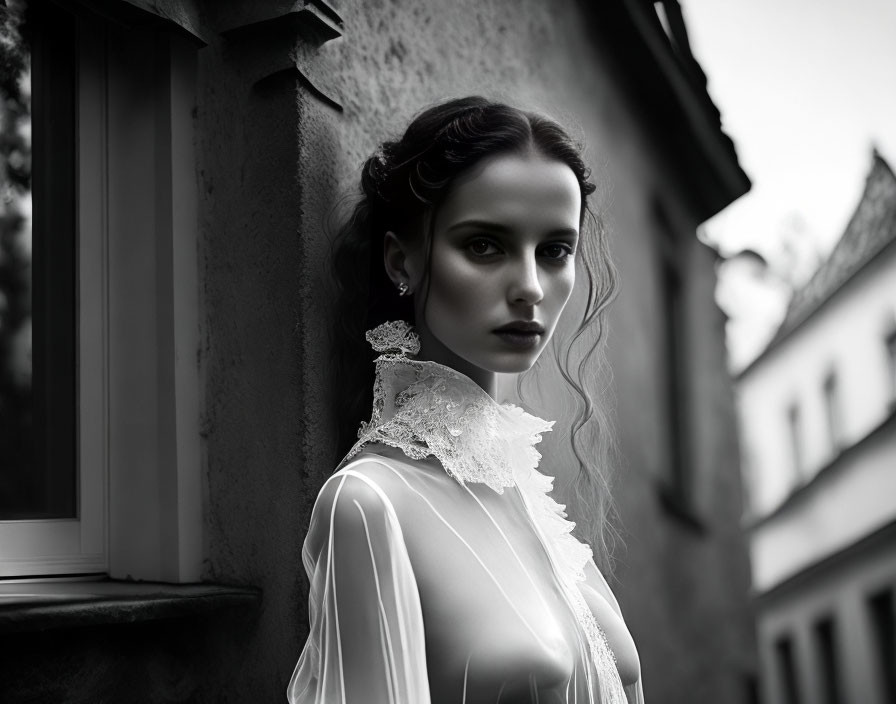 Monochrome portrait of woman in lace-collared dress by old building window