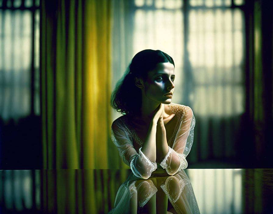 Contemplative person near window with yellow drapes in moody light