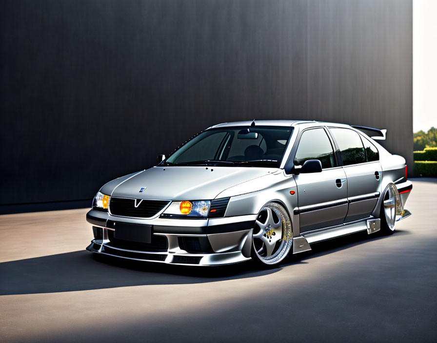 Customized silver sports sedan with low stance and aftermarket body enhancements parked against dark backdrop.