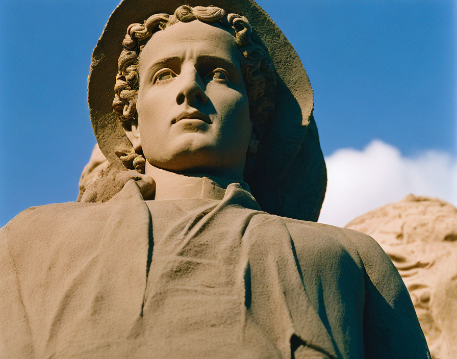 Figure statue with hat, draped clothing, and curly hair under blue sky