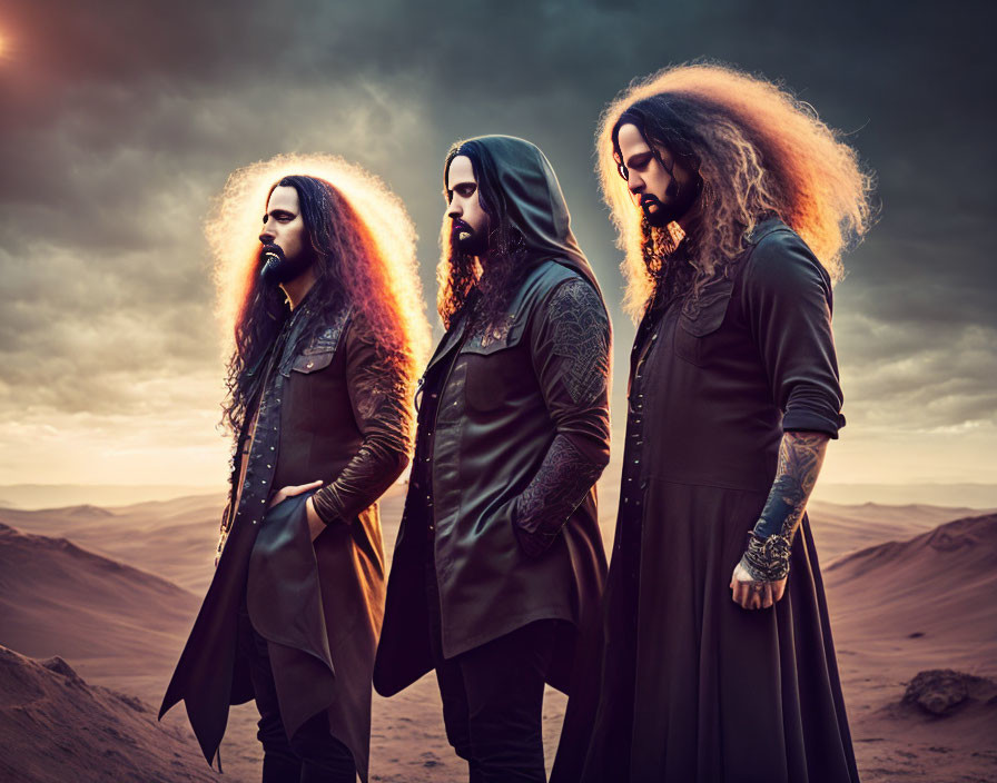 Three men with long hair and beards in black attire standing in a desert at dusk.