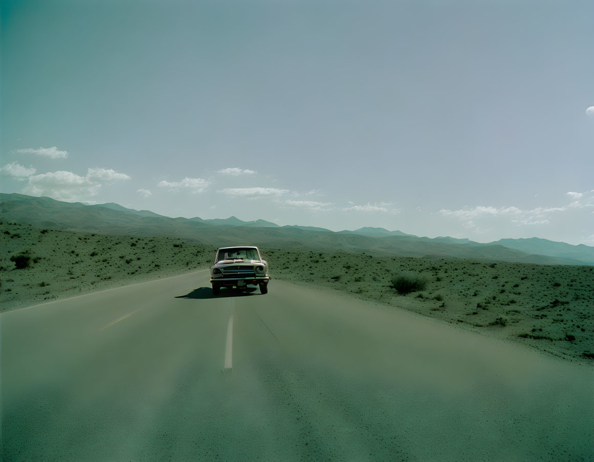 Vintage car cruising through barren landscape under clear sky