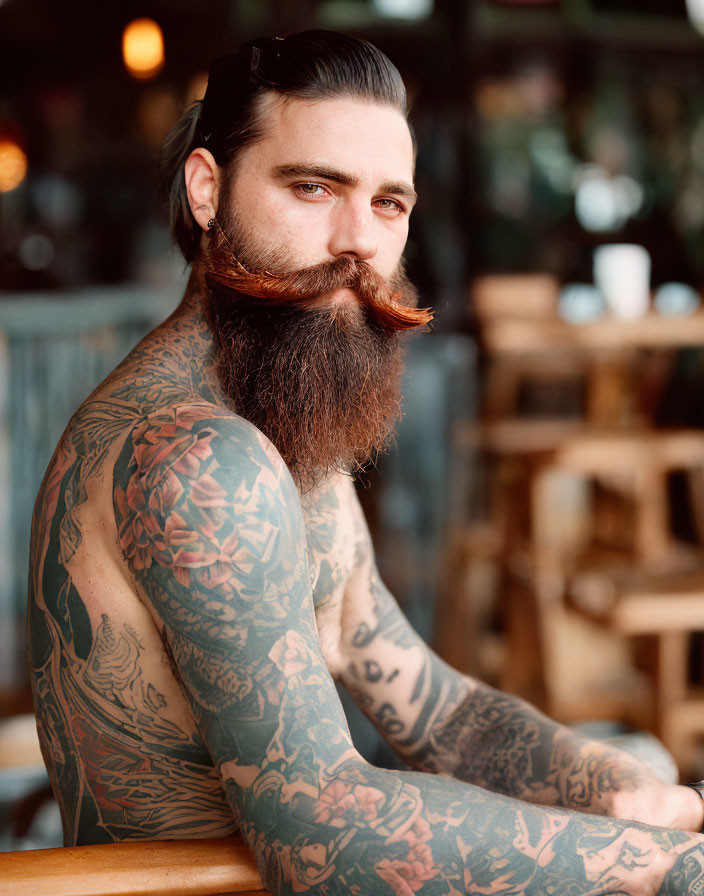Bearded man with tattoos sitting at cafe, gazing at camera
