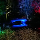Nighttime garden painting with bridge over pond, red and blue flowers, lush green foliage, dark blue