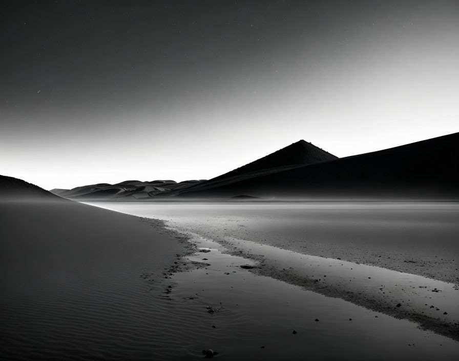 Monochrome sand dunes under starry sky with footprints on reflective surface