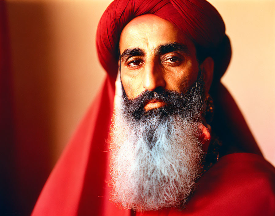 Bearded man in red turban and cloak against red backdrop