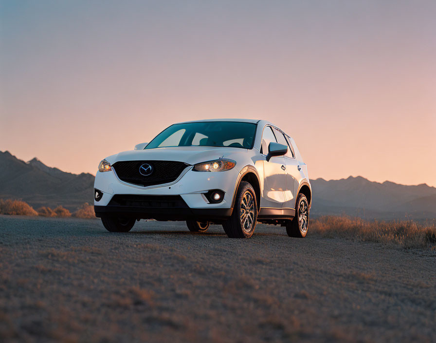 White Mazda SUV parked on dirt road with sunset mountains.