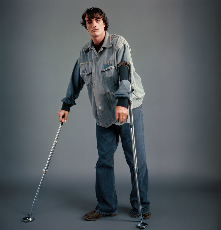 Person in oversized denim outfit standing with crutch