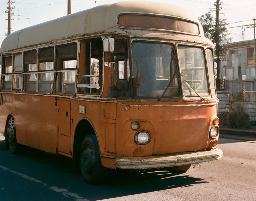 Weathered orange bus with cracked windows and rust spots parked on street beside buildings.
