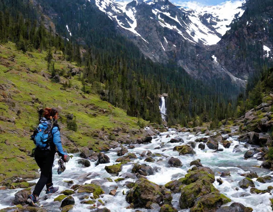Hiker walking by mountain stream with waterfall & snow-capped peaks