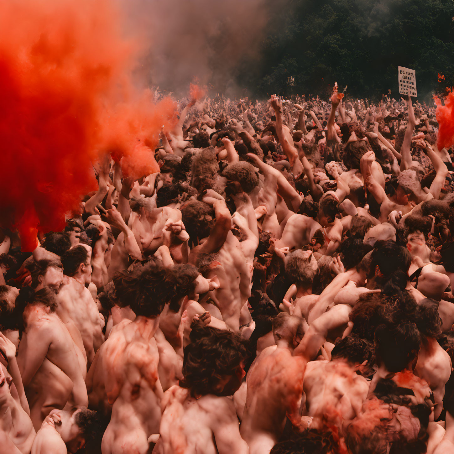 Crowded gathering in orange smoke with shirtless people and raised arms