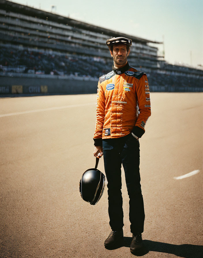 Racing suit man with sponsor logos on racetrack with grandstands