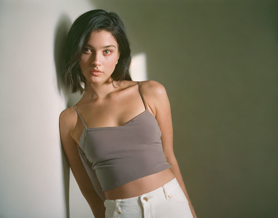 Young woman in cropped top and high-waisted pants gazes at camera