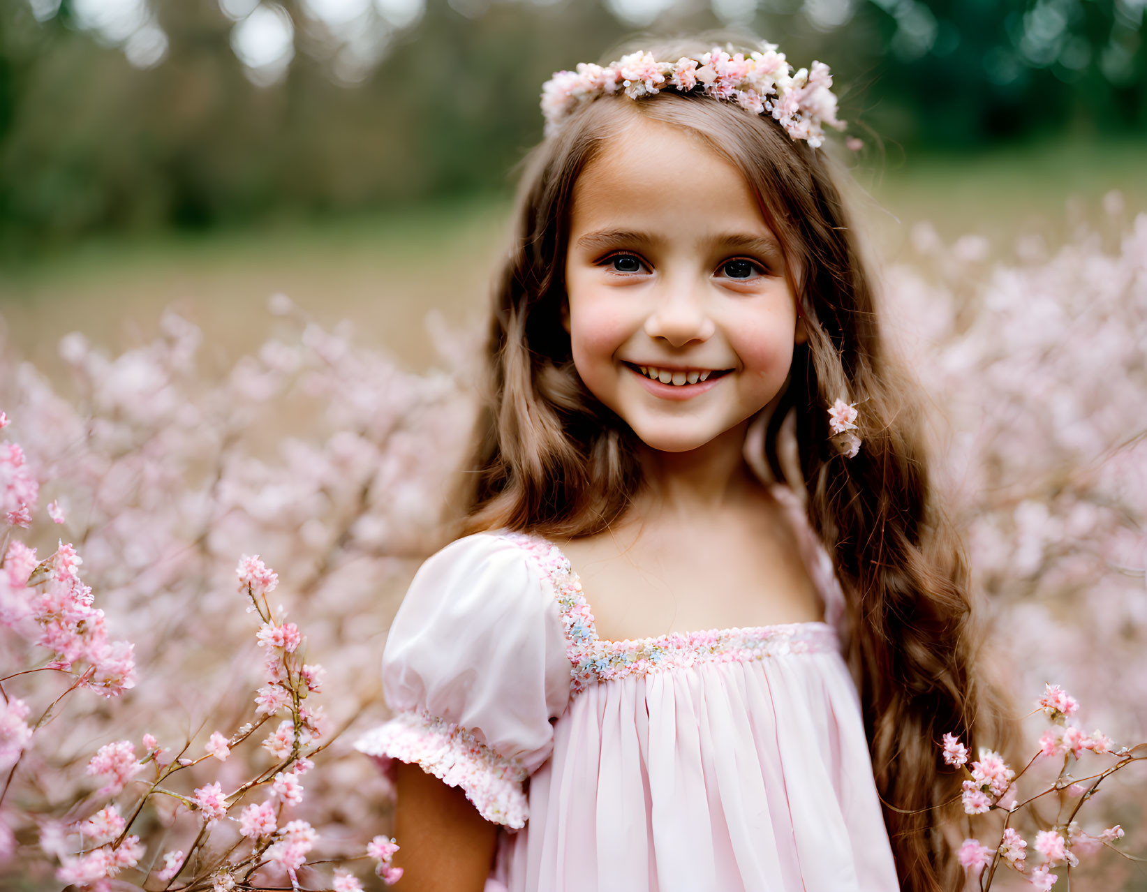 Young girl with floral headband in pink flower field smiling in pink dress