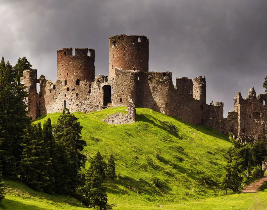 Medieval castle ruins on green hill under dramatic sky