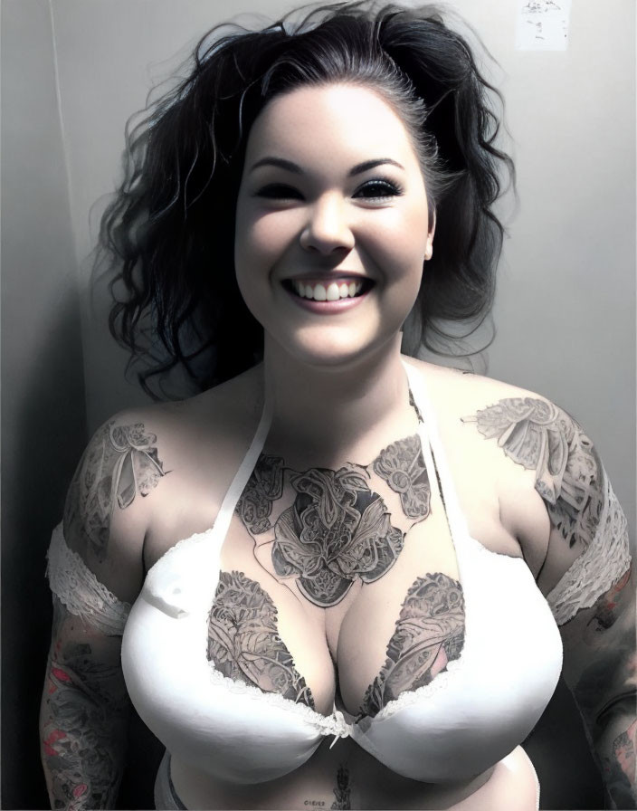 Smiling woman with dark hair and tattoos in white top