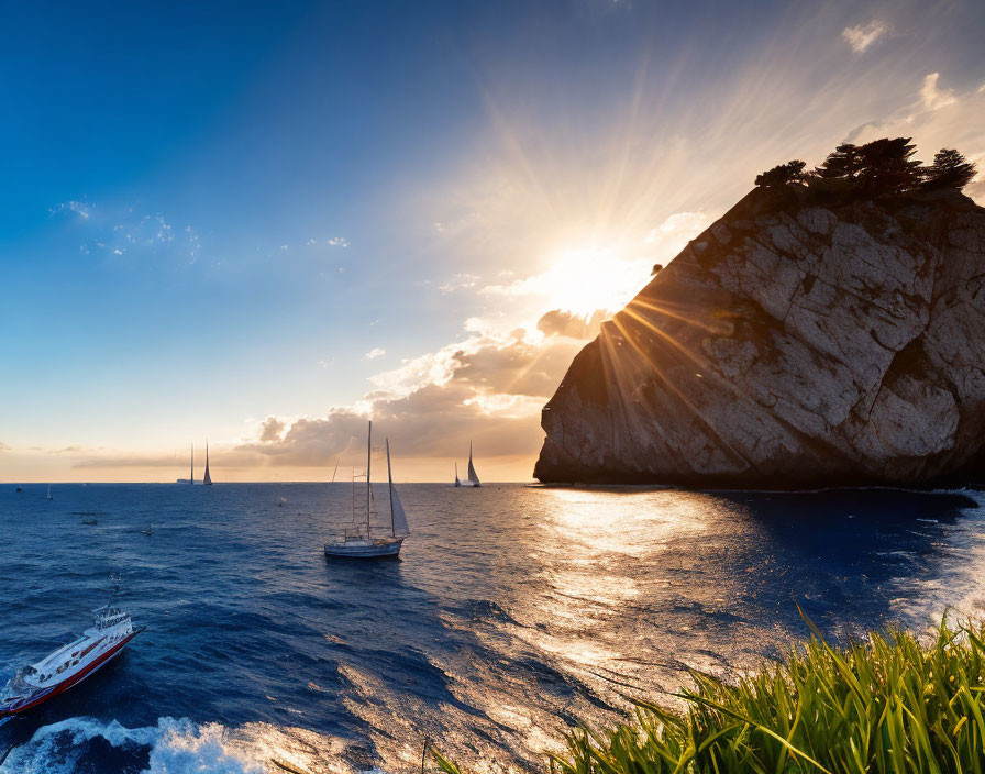 Sunset sailboats near large cliff with sun rays on blue sea.