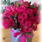 Pink roses and assorted flowers in blue vase with pink ribbon on soft-focus background
