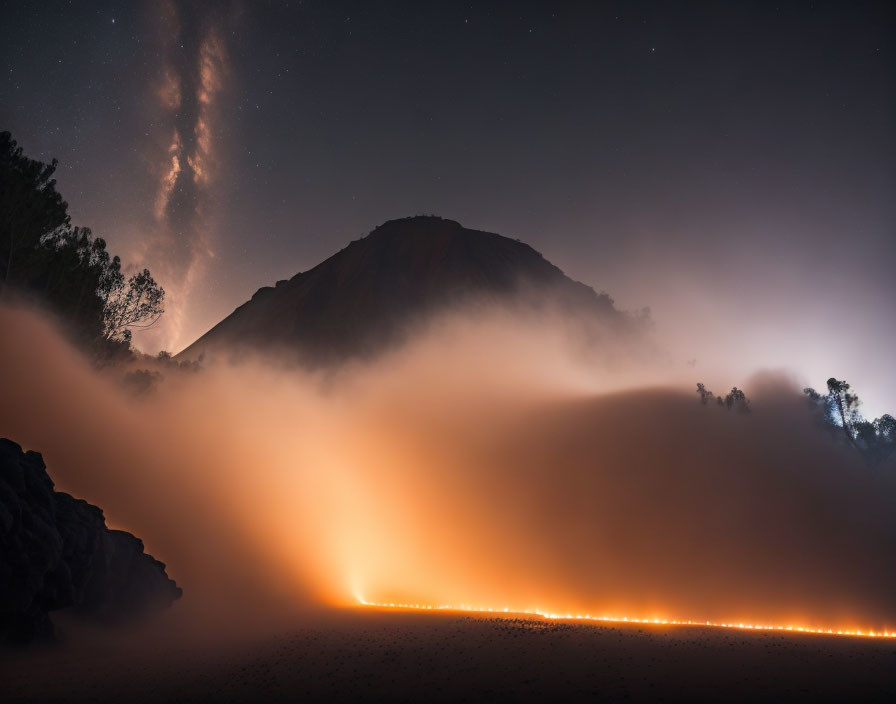 Starry Milky Way over mountain with orange lights in foggy night