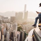 Person sitting on high ledge with cityscape backdrop at hazy sunrise