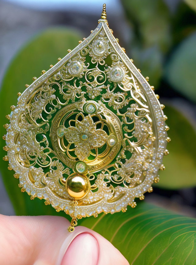 Intricate gold filigree earring with gemstones on leafy backdrop
